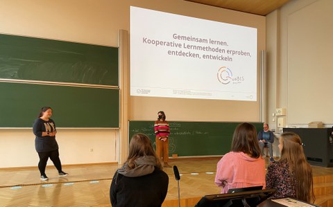 Zwei Referent:innen von QuaBIS stehen auf einer Bühne und geben ein Seminar für Studierende.