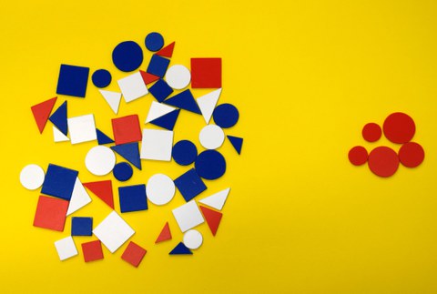 Auf dem Bild sind auf der linken Seite Kreise, Dreiecke und Vierecke in verschiedenen Farben in einem Gemenge zu sehen. Auf der rechten Seite sieht man nur rote Kreise. Sie sind separiert und das steht für den Begriff Exklusion.