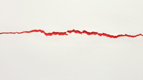 Crack in white surface with a red background exposed underneath. 
