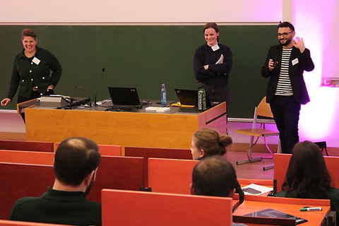 3 Personen vor einer Tafel die lachen und reden und präsentieren