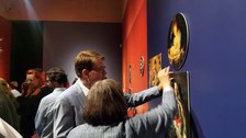 Director Prof. Dr. Holger Jacob-Friesen and a woman are standing in front of a dark blue exhibition wall. They are picking up one of the removable pictures.
