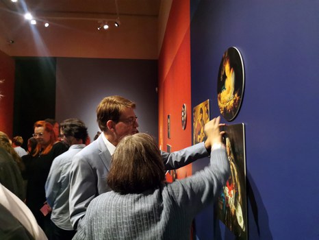 Director Prof. Dr. Holger Jacob-Friesen and a woman are standing in front of a dark blue exhibition wall. They are picking up one of the removable pictures.
