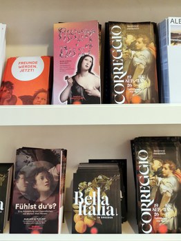 Various flyers for exhibitions at the Dresden Zwinger are displayed on a light-colored shelf.