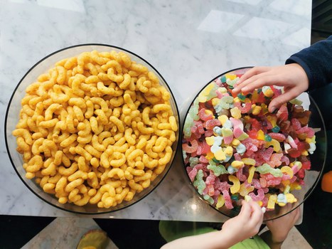 Two large bowls filled with colorful gummy bears and peanut flips. Two children's hands reach for the gummy bears.