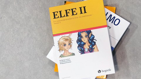 Auf einem Stapel liegen Ordner mit Unterhebungsmaterialien. Auf gelbem Grund der Titel "ELFE 2. Ein Leseverständnistest", darunter auf weißem Grund zwei Comicfiguren im Mangastil.