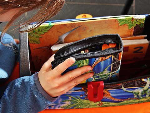 Eine Kinderhand hält eine bunte Federtasche vor einem Schulranzen.