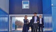 Schulleiterin Maxi Heß und Kultusminister Conrad Clemens laufen vor dem blauen Containerbau der Universitätsschule Dresden.