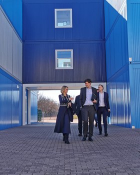 Schulleiterin Maxi Heß und Kultusminister Conrad Clemens laufen vor dem blauen Containerbau der Universitätsschule Dresden.