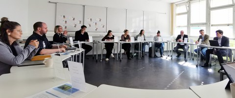 An einem großen Tischkreis sitzen bei einer Diskussion die Mitglieder der Erweiterten Schulleitung der Universitätsschule Dresden, Vertreterinnen des Schülerrats, des Elternrats, Landeselternsprecher Ronald Lindecke, ein Vertreter des LaSuB und Kultusminister Conrad Clemens.