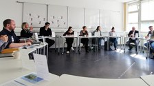 An einem großen Tischkreis sitzen bei einer Diskussion die Mitglieder der Erweiterten Schulleitung der Universitätsschule Dresden, Vertreterinnen des Schülerrats, des Elternrats, Landeselternsprecher Ronald Lindecke, ein Vertreter des LaSuB und Kultusminister Conrad Clemens.
