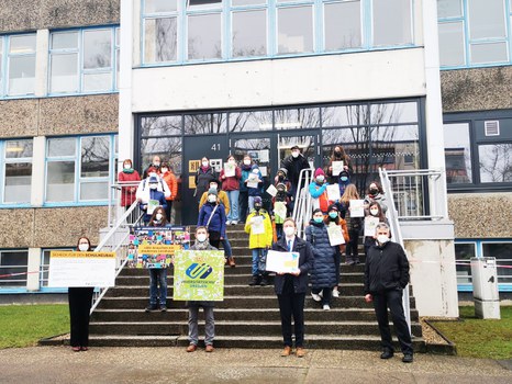 Auf der Treppe vor dem Schulgebäude steht die Delegation mit dem Spendenscheck, Million-Pixel-Bild und der Mappe mit den Unterschriften
