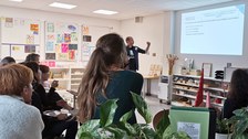 Eine Workshop-Gruppe schaut auf einen Lernbegleiter. Er erklärt ein an die Wand projiziertes Schaubild.