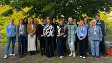 17 Personen stehen unter einem herbstlich gefärbten Baum und lachen in die Kamera.