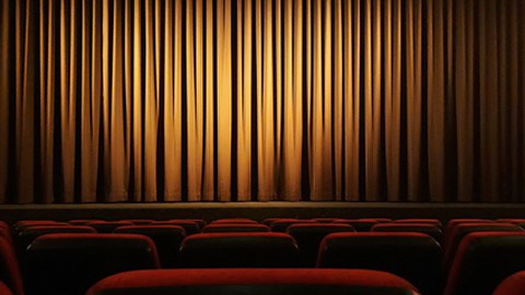 The picture shows part of an empty movie theater in semi-darkness, with the curtain closed.