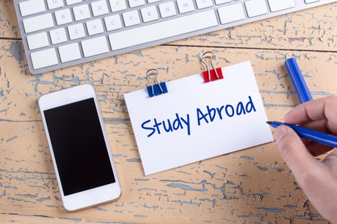 Das Foto zeigt einen Tisch. Darauf liegt eine Computertastatur, ein Handy und ein Notizzettel mit der Aufschrift "Study Abroad"