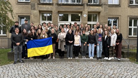 Student:innen aus der Ukraine und Deutschland stehen vor einem brauen Universitätsgebäude. Drei Studenten halten eine Ukraine-Flagge hoch
