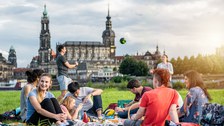 Gruppe von Studenten an der Elbe. Sie spielen Volleyball und sitzen plaudernd auf der Wiese