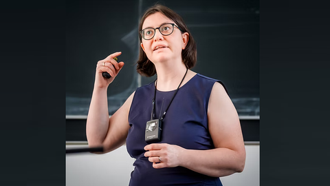 Professor Caroline Murawski gestures while answering a question in front of the blackboard.