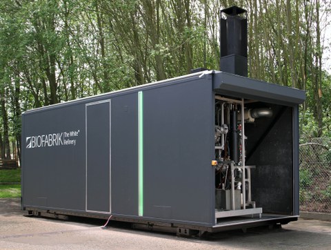 Gray container representing modular plant stands on asphalt ground, in the background there is a fence and trees.