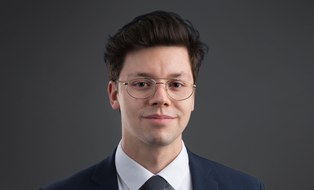 Mann mit dunklen Haaren und Brille, gekleidet in Anzug und Krawatte