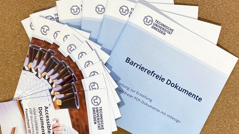 Broschüren und Flyer, aufgefächert auf dem Tisch, Anleitungen zur Erstellung barrierefreier Dokumente.