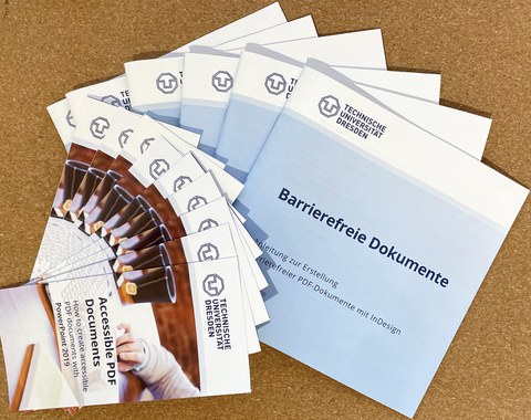 Broschüren und Flyer, aufgefächert auf dem Tisch, Anleitungen zur Erstellung barrierefreier Dokumente.