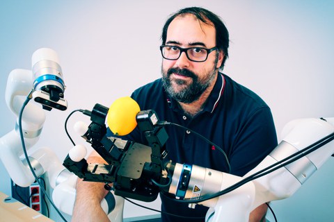 Prof. Robert Calandra mit zwei Roboterarmen, welche eine  Roboterhand mit ergriffener Zitrone und eine Kamera tragen