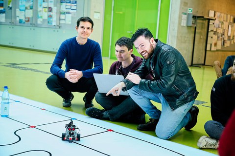 drei Studenten beim RoboLab im Foyer der Fakultät Informatik mit Planet und Legoroboter im Vordergrund
