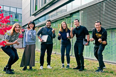 6 internationale Studierende nebeneinander mit "Begeisterungsgeste" neben dem APB