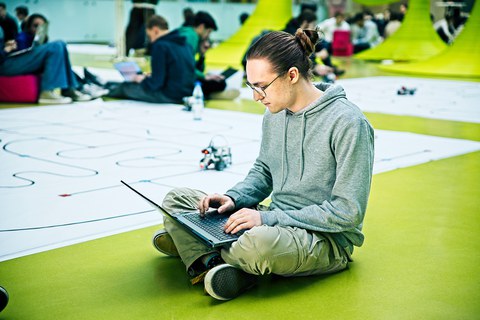 Student mit Laptop vor Planeten des RoboLabs im Foyer des APB sitzend