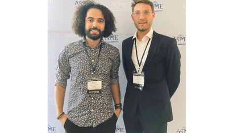 Herr Guesmi und Herr Manthey, nebeneinander stehend und lächelnd, bei der Konferenz.