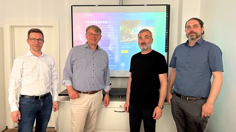 4 Männer schauen nach dem Meeting für ein Gruppenfoto in die Kamera, hinter Ihnen die Website von Pro3 mit der geöffneten Unterseite der TU Dresden.
