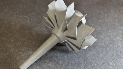 The photograph shows a ceramic turbine wheel, being complexely shaped and of light-grey colour.