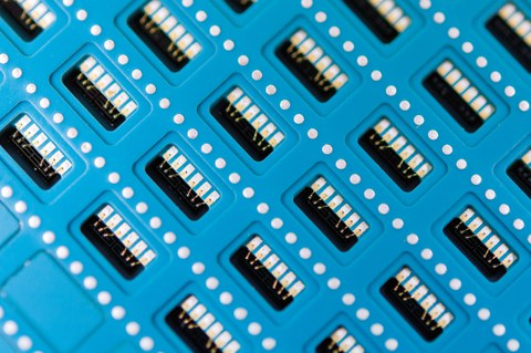 Closed view on the surface of a stack of blue-coloured LTCC ceramic. The ceramic foils include a big number of identical micro-electro-mechanical systems.