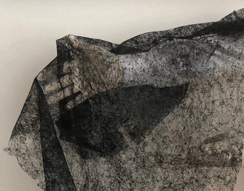 Thermoplastic fleece: Photo of the material laid over an arm. Material has a net-like structure, semi-transparent, in black