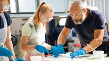 Ingenieur erklärt einem Mädchen das Laminieren und zeigt auf die Laminiermasse