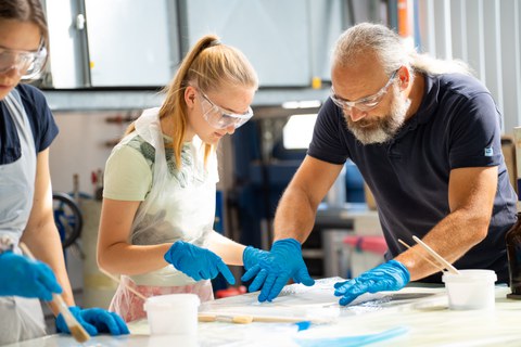 Ingenieur erklärt einem Mädchen das Laminieren und zeigt auf die Laminiermasse