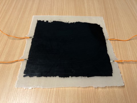 Auf einem Tisch liegt eine Platte, die aus zwei verschiedenen Schichten besteht: Die äußere, größere ist halbtransparent und bildet den Rahmen für die zweite, dunklere Schicht.