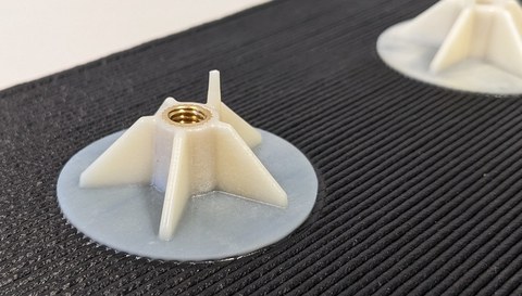 Plastic part tapering towards the top, which is moulded in one piece on a round plate. At the upper end there is an opening with a metal thread that leads into the inside of the part. 