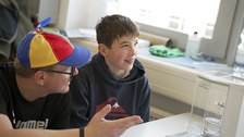 A technician explains something to a boy. The boy looks up into the air and seems to be thinking. In front of him is a density meter.