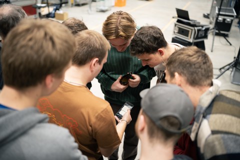 Students stand in a circle and look at a smartphone. They are taking the online quiz.