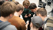 Students stand in a circle and look at a smartphone. They are taking the online quiz.