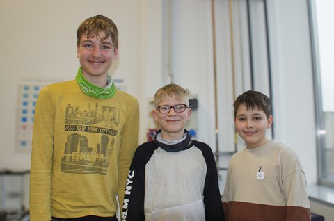Three boys aged around 11 to 13 smile at the camera.
