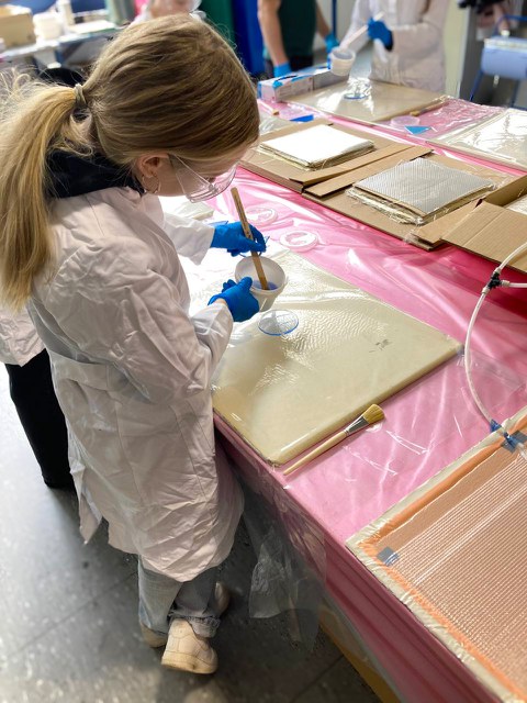 A girl doing hand lamination: She pours a blue, semi-transparent liquid from a small bucket onto a base. At the same time, she holds a wooden stick in her hand.