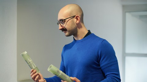 A man with glasses and a bald head looks at the components he is holding in his hand.