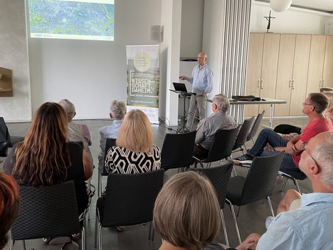 Prof Dr Modler giving a lecture, with the guests sitting in the foreground listening to the speaker. In the background: a PowerPoint presentation projected onto the wall.