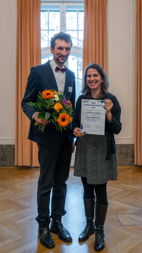 Two people, a man and a woman, smile at the camera and hold up a certificate.