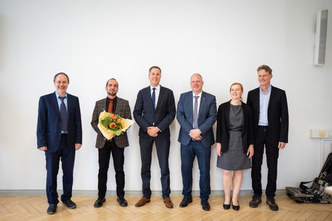 Six people stand next to each other and look smiling into the camera. The second person from the left is Robert Kupfer. He is holding a bouquet of flowers.