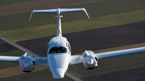 Frontalaufnahme eines Flugzeuges im Flug. Im Hintergrund Ackerland.