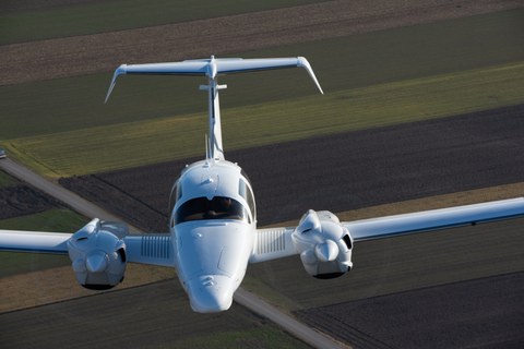 Frontalaufnahme eines Flugzeuges im Flug. Im Hintergrund Ackerland.